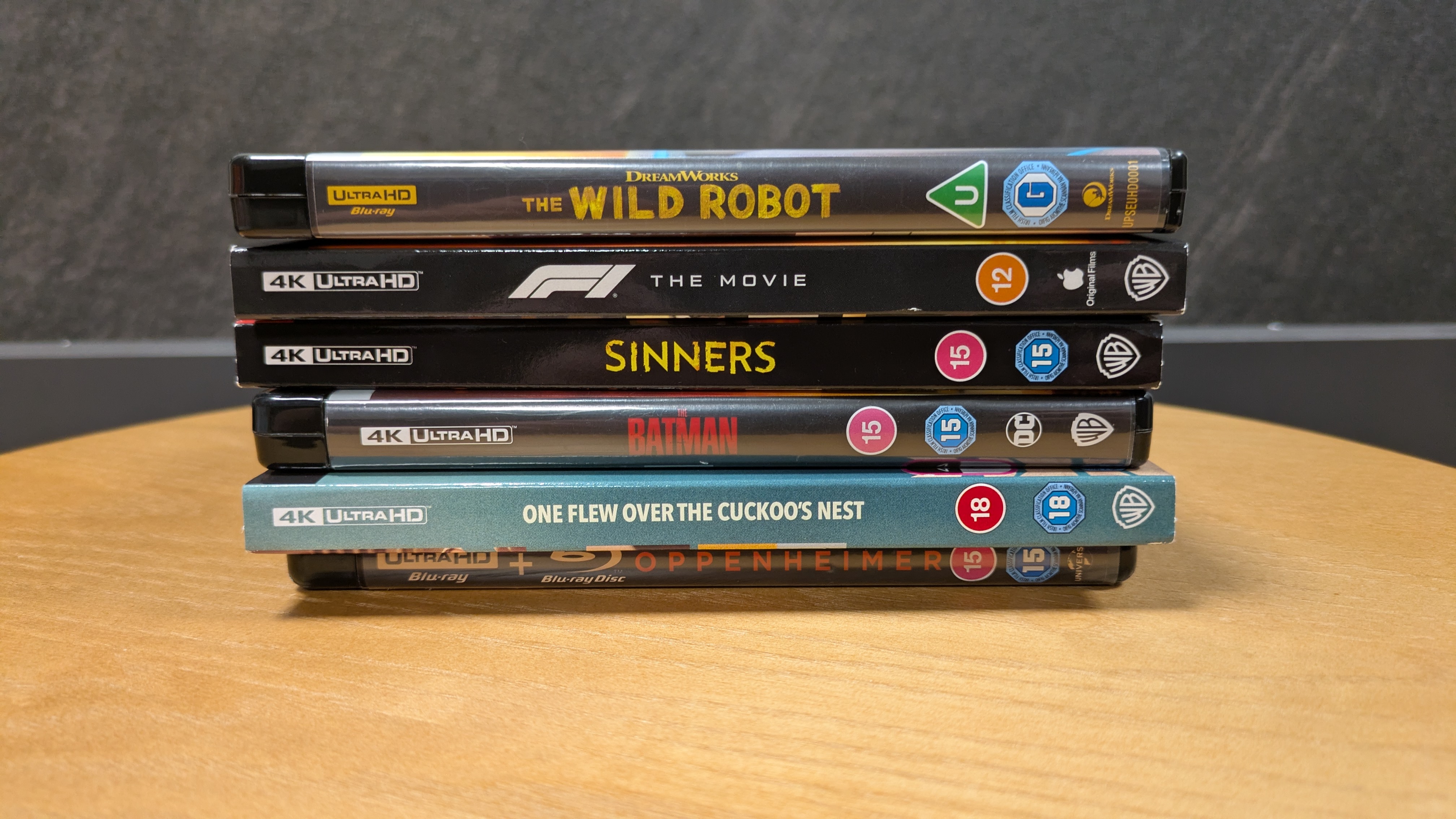 4K Blu-ray cases of The Wild Robot, F1, Sinners, The Batman, One flew over the cuckoo's nest and Oppenheimer all stacked in pile, spine side facing camera