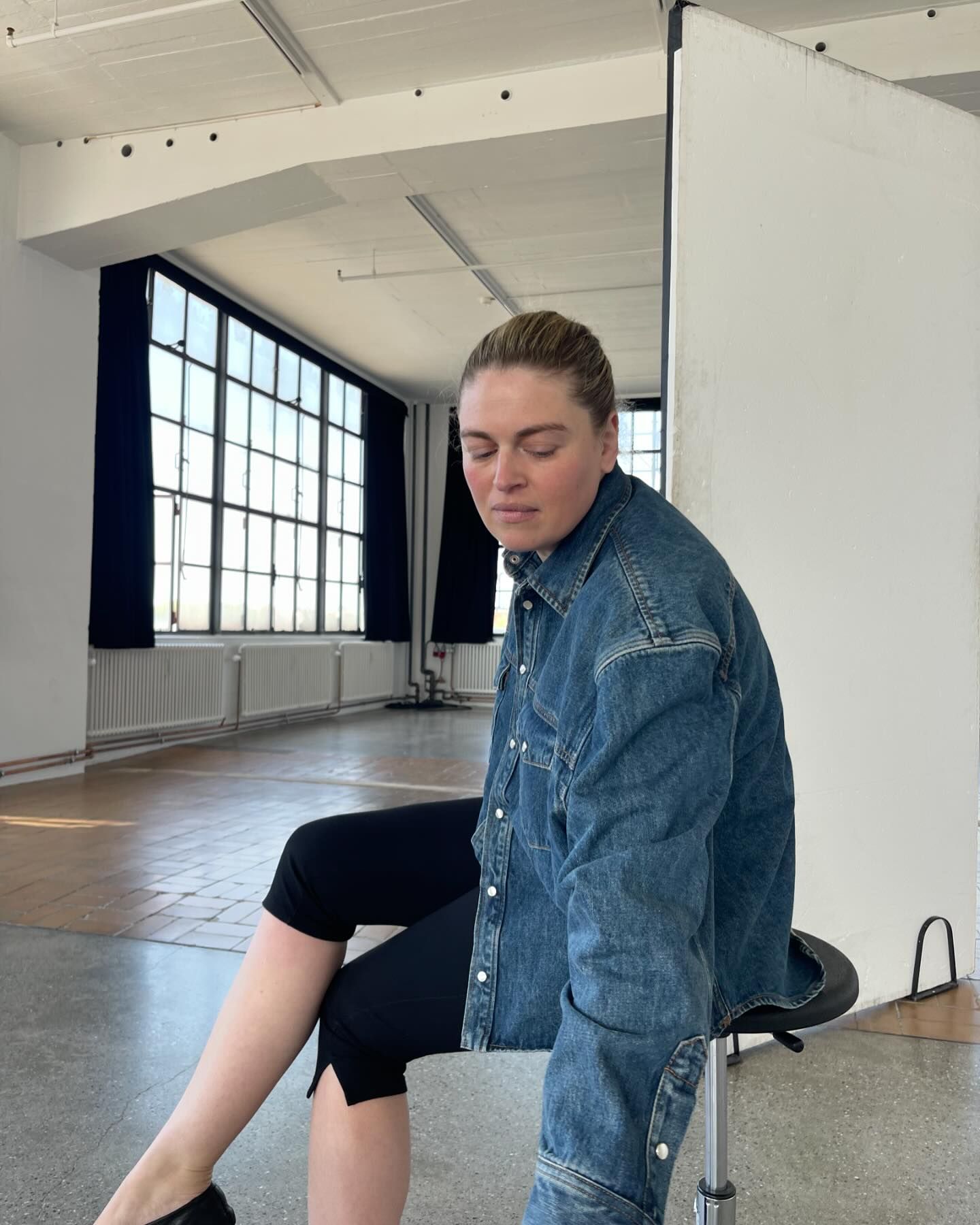 Danish fashion creative Sidsel Alling poses in a studio in Copenhagen wearing a denim jacket, slit-hem black capri pants, and black flats