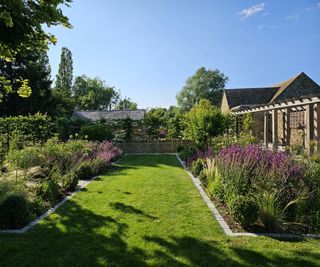 A traditional garden with large planting beds and a lawn with wooden pergola walway