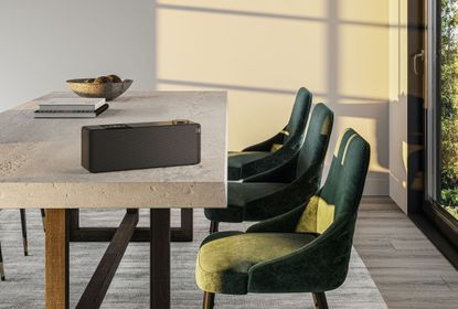 a speaker sitting on top of a concrete slab dining table with wooden legs, paired with three green felt chairs
