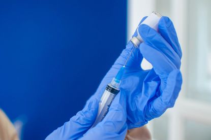 A young doctor in blue protective glove is holding a medical syringe and vial