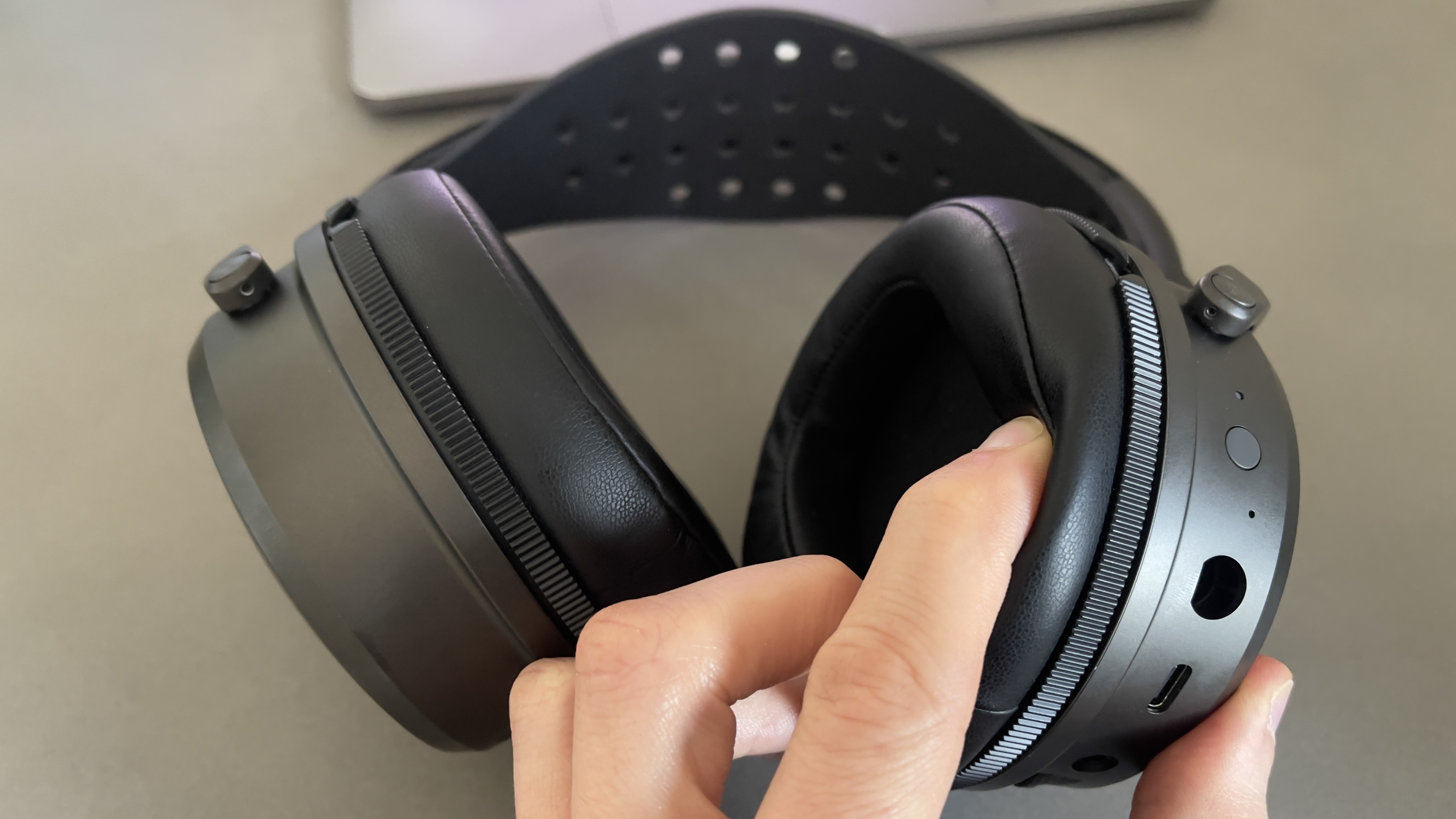 The Audeze Maxwell 2 gaming headset lying on a pale desk with a hand tweaking an ear cushion