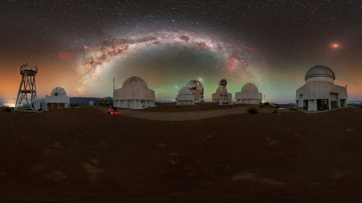 A bunch of white-domed observatories under the starry sky. The Milky Way&#039;s heart arches over them all. To the right, the blood moon.