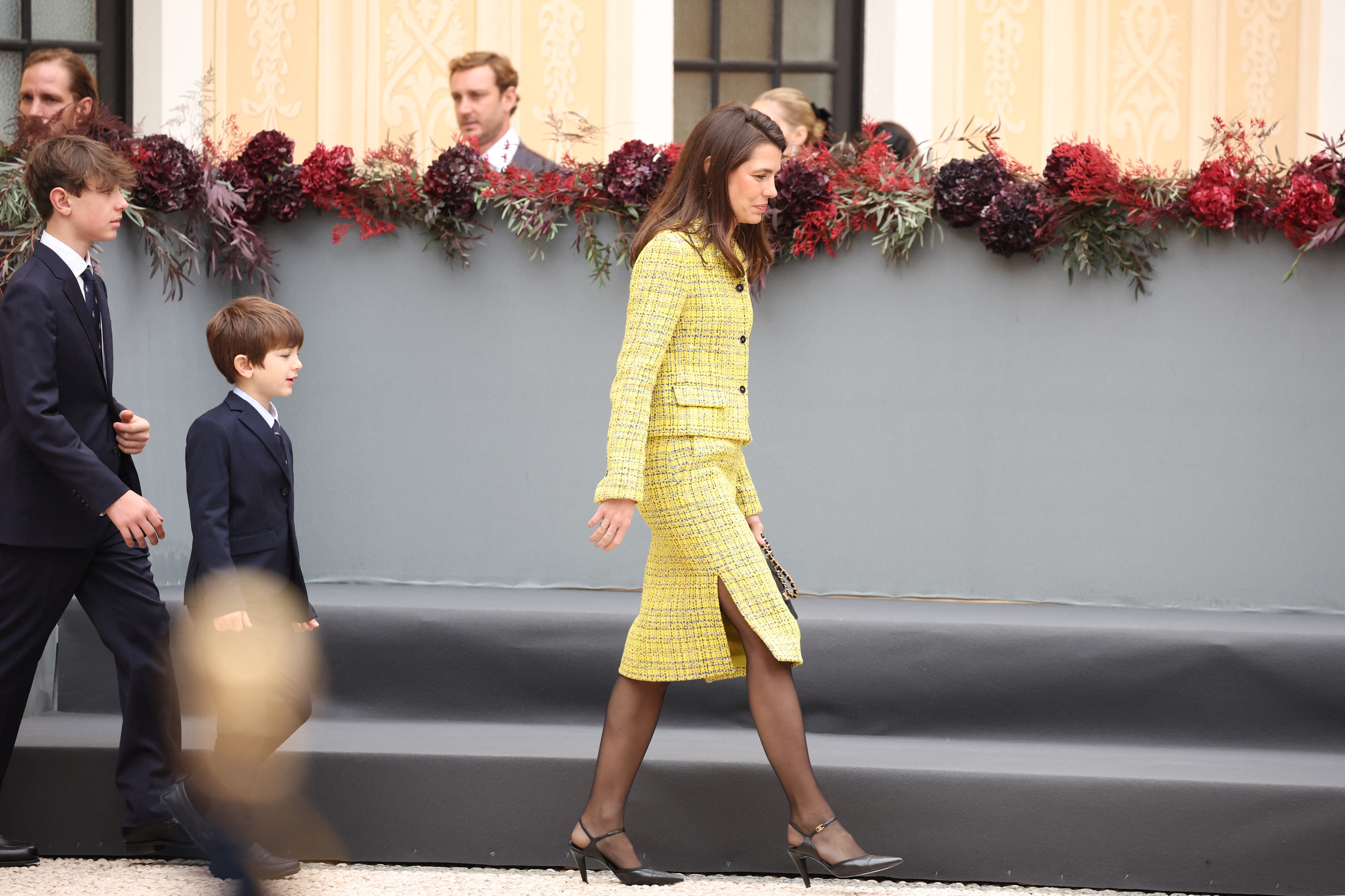 Charlotte Casiraghi wearing a yellow skirt suit walking in front of two boys
