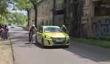 Screen grab of video showing two riders holding onto side of team car at Tour de Guadeloupe