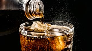 Close-up of fizzy soda being poured into a drinking glass filled with ice against a black background.