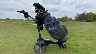 The black and navy Motocaddy Cart Series Bag mounted on a trolley on the golf course