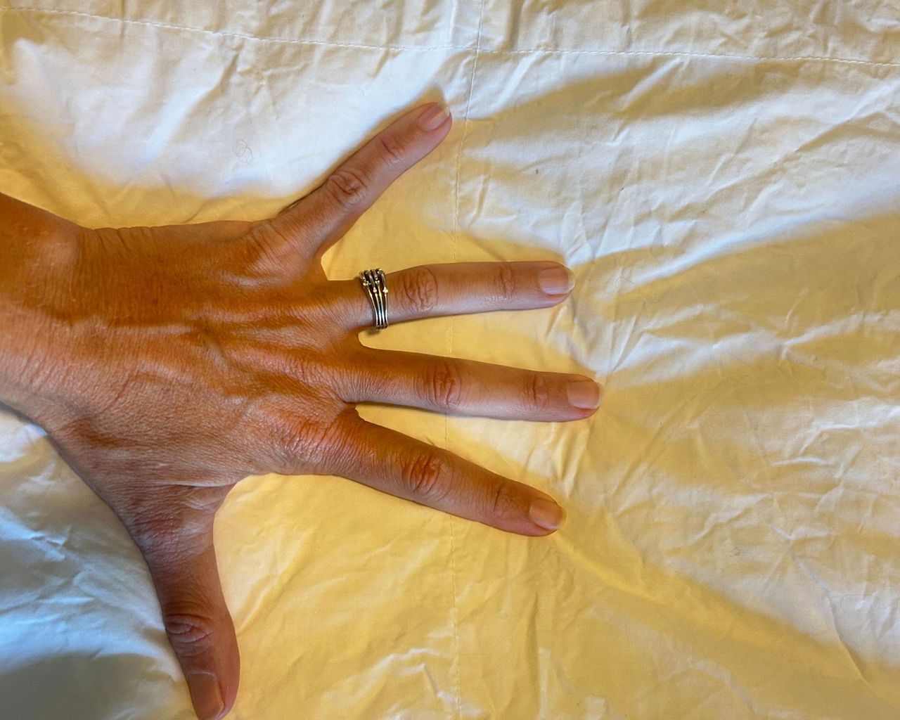 A woman's hand pressing into a white duvet. There is a silver ring on her ring finger, and her fingers are spread to test the loft of the Boll &amp; Branch Down Alternative Duvet Insert.