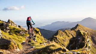 A mountain bike rider on mountainous singletrack wearing an Osprey Raptor 14 hydration pack