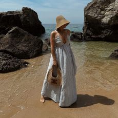 woman on beach with a flowy summer maxi dress, straw hat, and straw bag