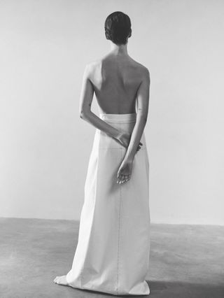 Woman in white Fforme skirt and no top facing away from the camera