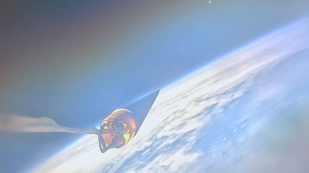 a dark, triangular rocket nose cone is seen in space above the curve of Earth