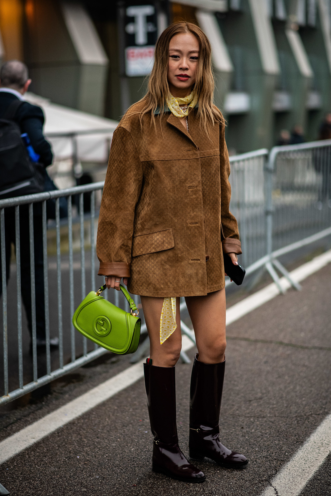 Milan fashion week attendee wearing a suede jacket and knee high boots green gucci bag