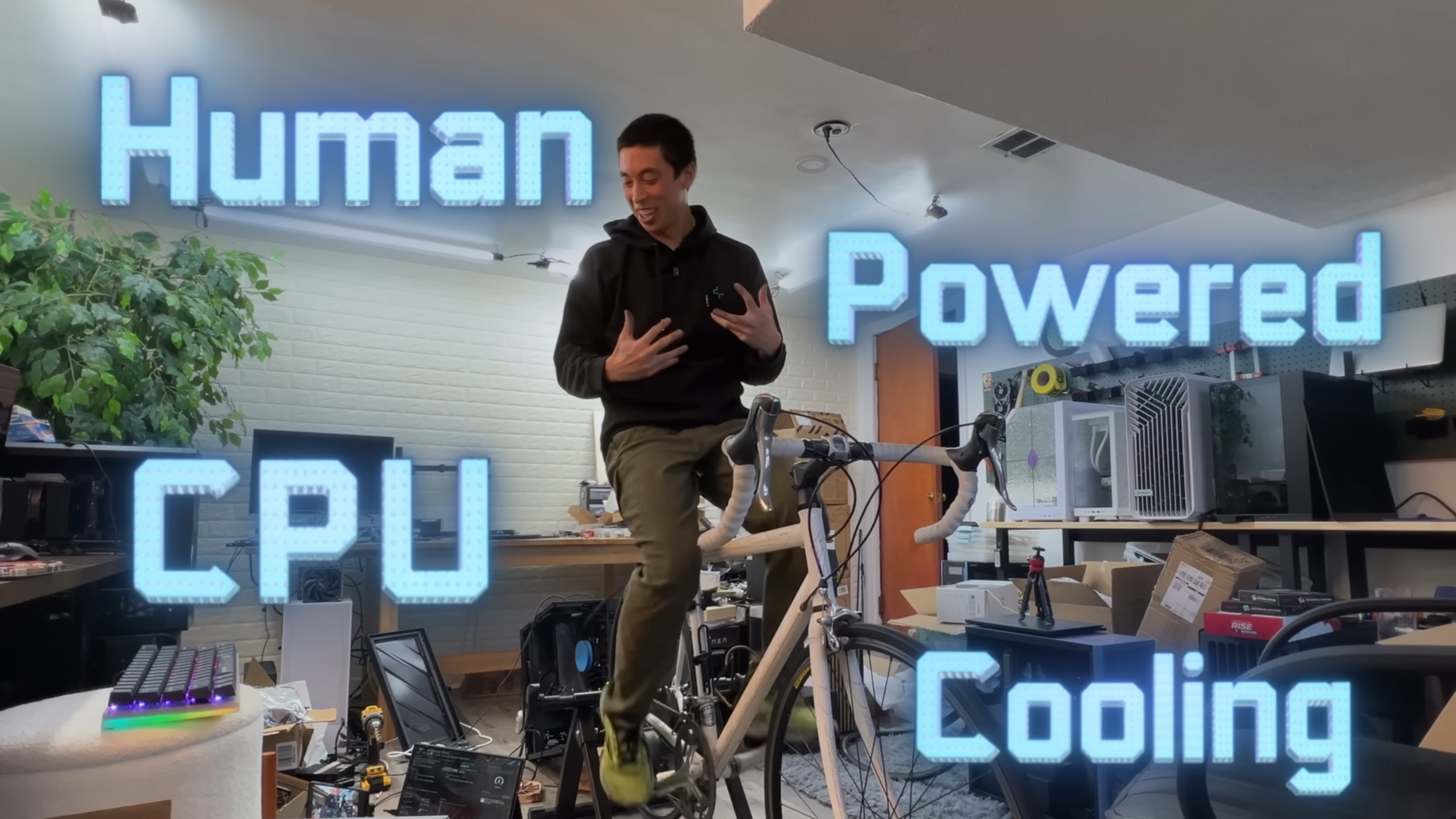 A YouTuber sits on a bike that he is pedalling in order to turn the fan on his CPU.