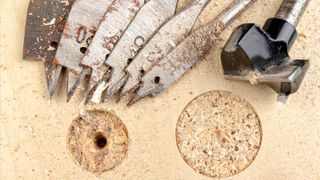 Spade and Forstner bits laid out on chipboard next to two cut holes