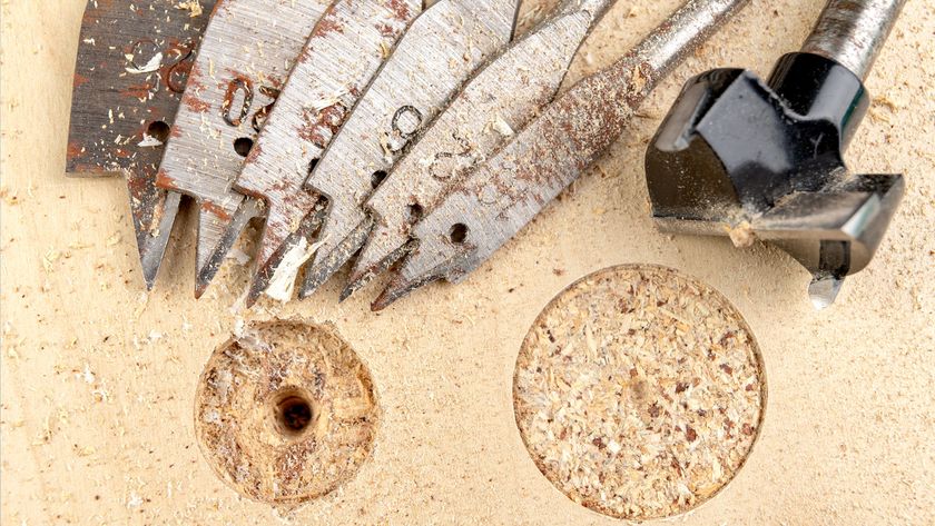 Spade and Forstner bits laid out on chipboard next to two cut holes 