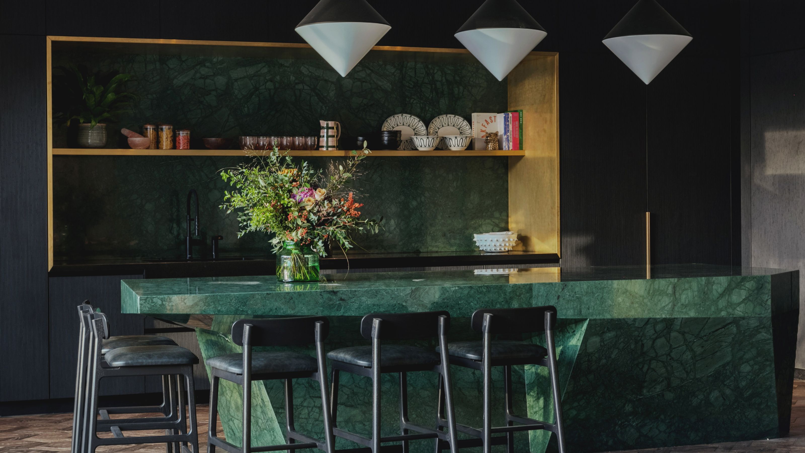 A kitchen island in green marble stone with bar stools beside it and pendant lights hanging above
