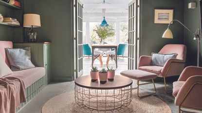 Living room with pink tropical wallpaper and green velvet sofa.