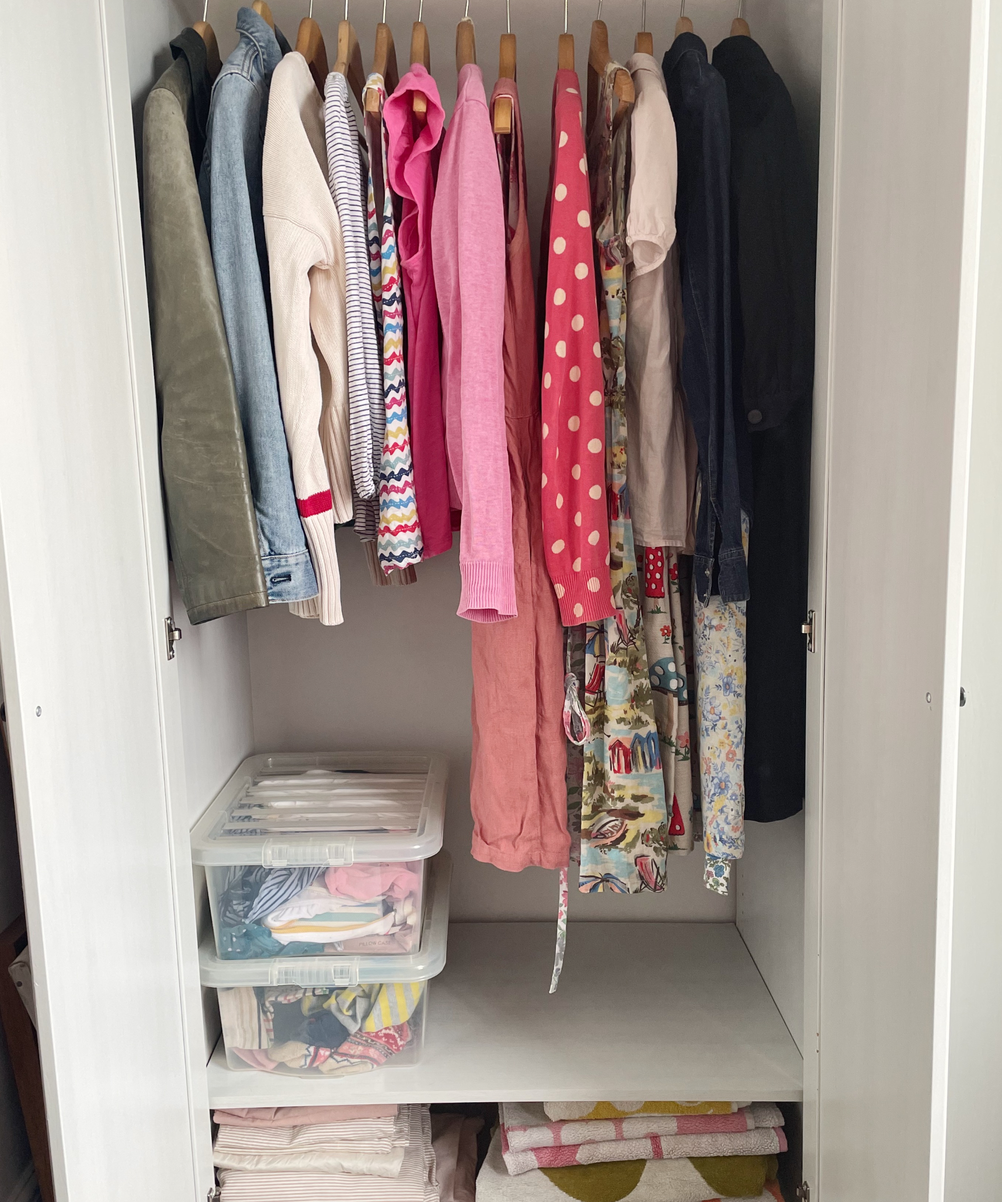 closet with hanging clothes neatly placed, clear storage bins, bedding and towels on shelving