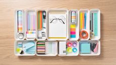 Neatly organized stationery in white trays on wooden desk viewed from above
