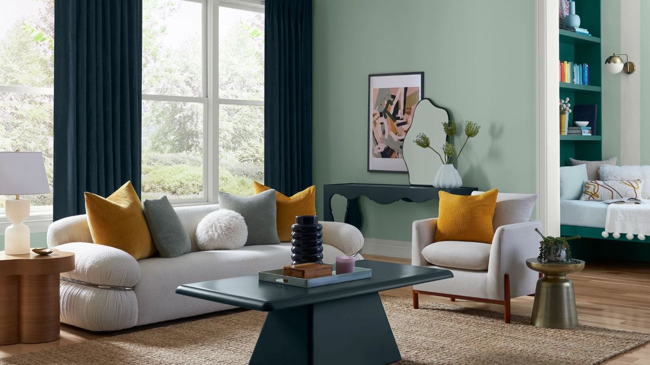 modern living room with pastel green walls dark green curtains, neutral rug and light gray sofa and armchair with yellow cushions