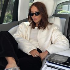 @deborabrosa wears a cream jacket, black trousers and silver shoes whilst sitting in the front of a car