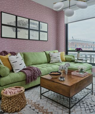 pastel living room ideas, living room with pastel pink wallpaper, green sectional, globe pendant light, artwork, vintage style coffee table