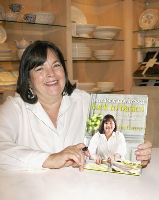 ina garten holds up a copy of her cookbook Barefoot contessa smiling