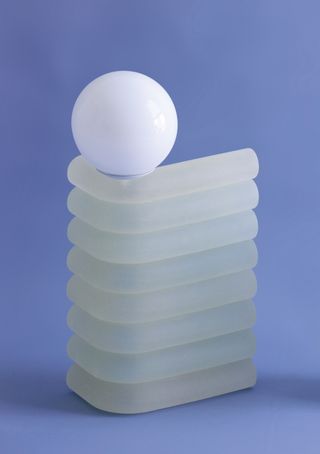 A table lamp with a base made of translucent sausage-like forms stacked on top of each other and a simple white spherical bulb by Soft Geometry