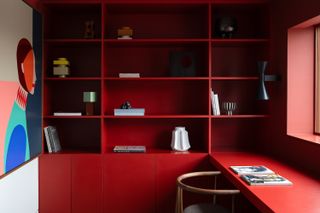 A red bookcase, cabinet and desk beside a colorful painting