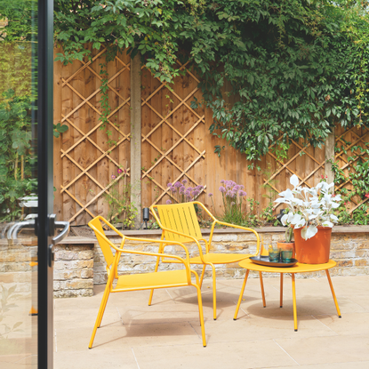 Pastel yellow garden table and two chairs on a patio.