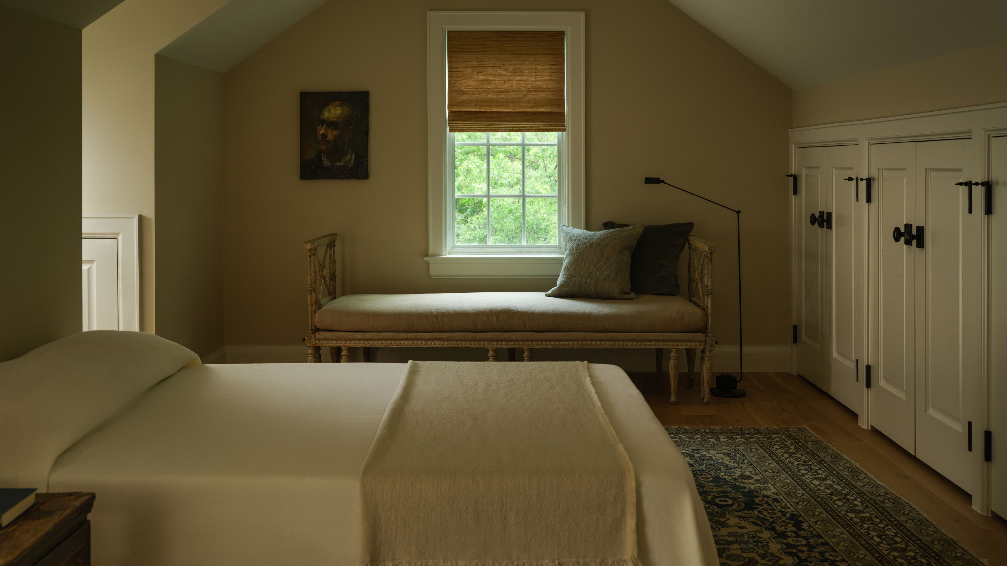 a warm beige attic guest bedroom with vaulted ceiling, eave storage, an antique window bench seat and neutral linens