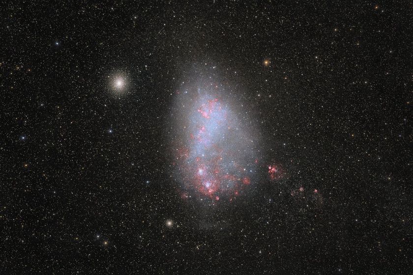 A black space background covered in stars has a central bright, egg-shaped galaxy with blue and red coloring. 