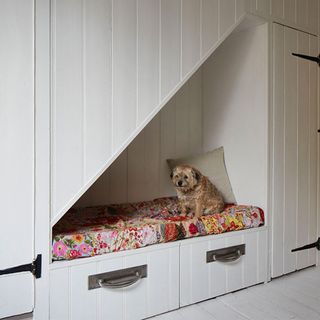 grey painted cupboard and drawers in under stairs storage area, with colourful cushion on bench seat with a small dog sitting on top