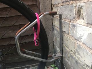 A pink Hiplok Z LOK COMBO securing rear bike wheel to wall-mounted rack