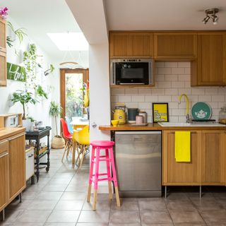 White open plan kitchen diner with wooden mid-century cabinets, tiled floor, yellow tap and skylight