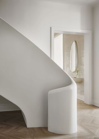 The curved staircase in the white hallway of an NYC apartment showing the beige bathroom behind