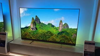 The Philips OLED+910 TV with a lush forest landscape and clear sky on the screen