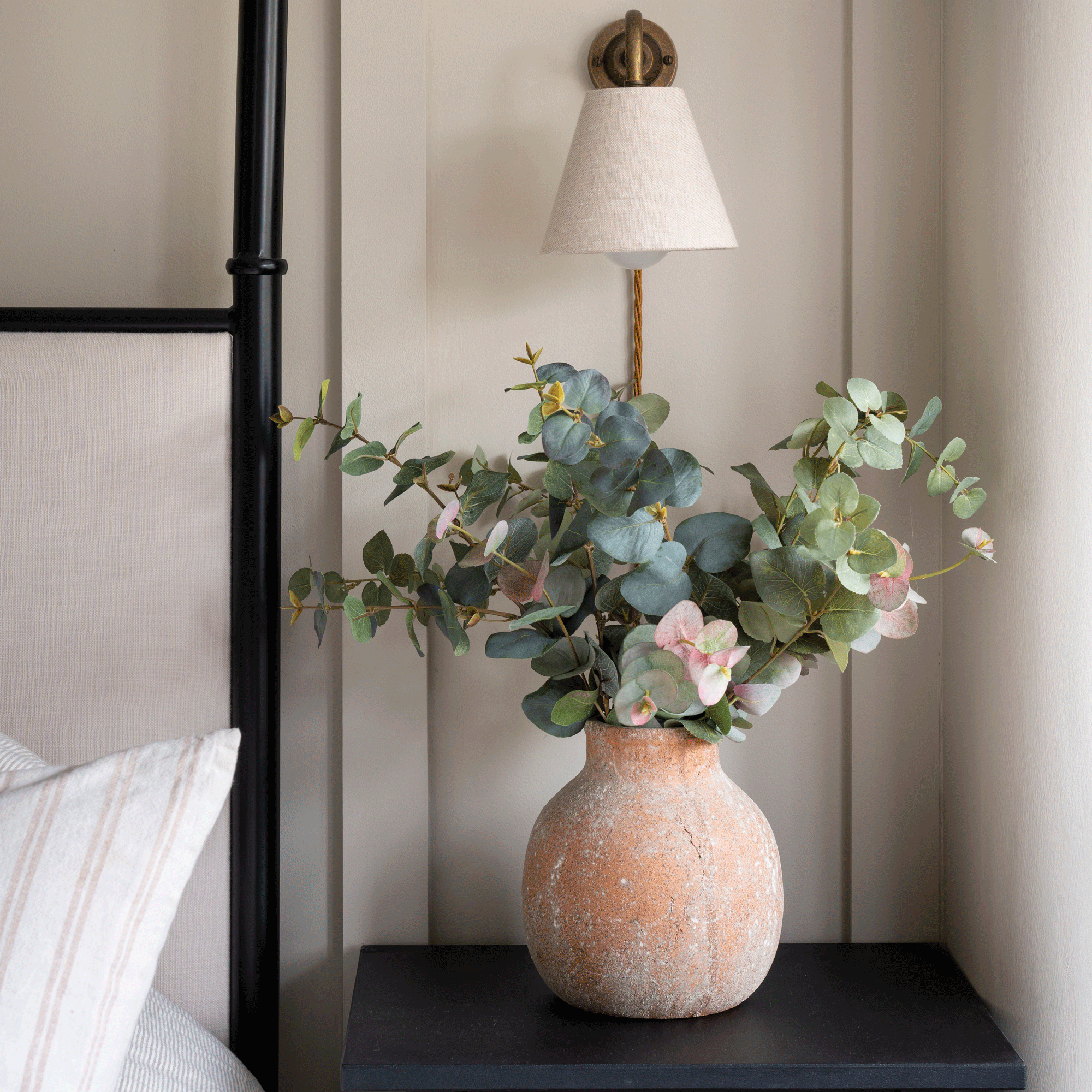 a bedroom with a black beside table with a terracotta vase filled with eucalyptus and flowers