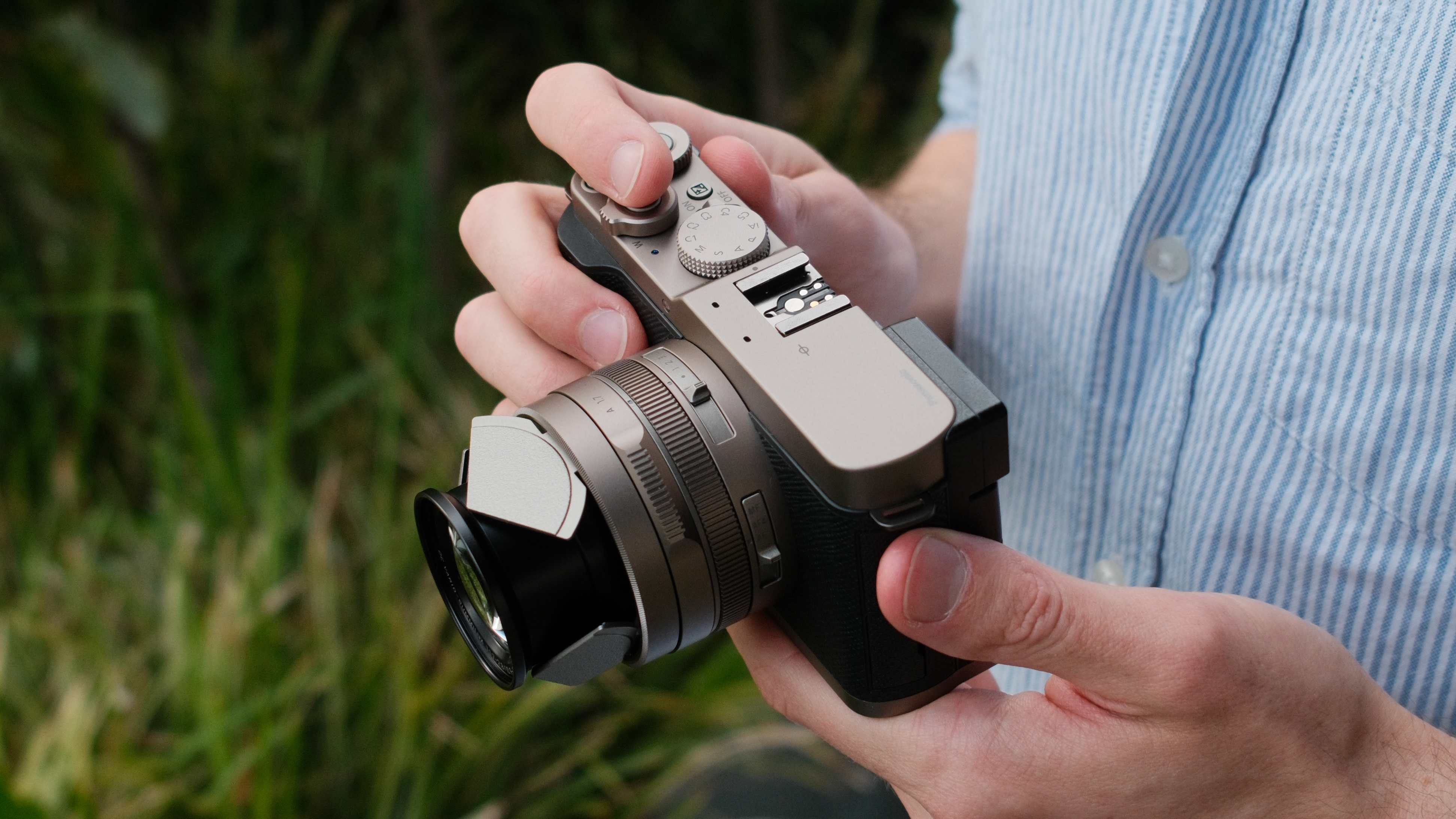 Hands holding the Panasonic Lumix L10 camera and adjusting its controls.