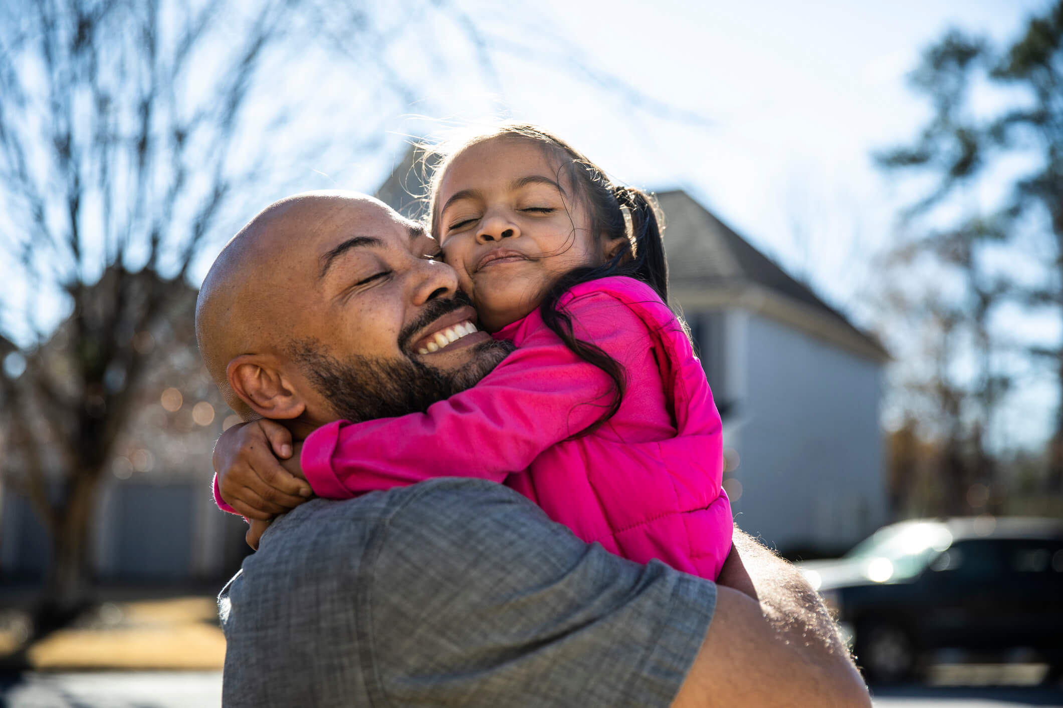 A dad is smiling whilst holding his daughter in an embrace 