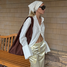 An image of a model wearing an embroidered bandana, a white button-down shirt and pale yellow satin trousers