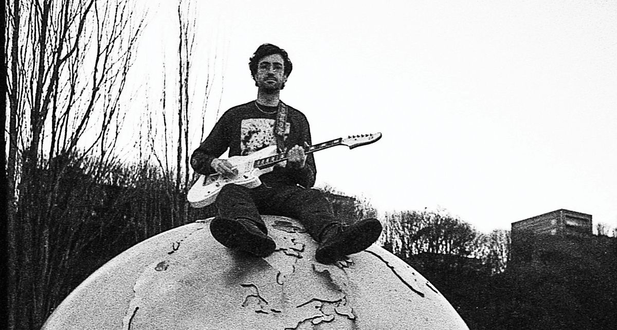 Max Keyes of Spiral XP sits on top of the world – at least a sculpture of it. The picture is grayscale black-and-white and he plays an offset guitar.