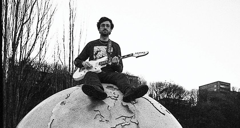 Max Keyes of Spiral XP sits on top of the world—at least a sculpture of it. The picture is grayscale black-and-white and he plays an offset guitar.