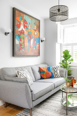 Living room with white walls, grey fabric sofa, black geometric ceiling light and colourful statement artwork