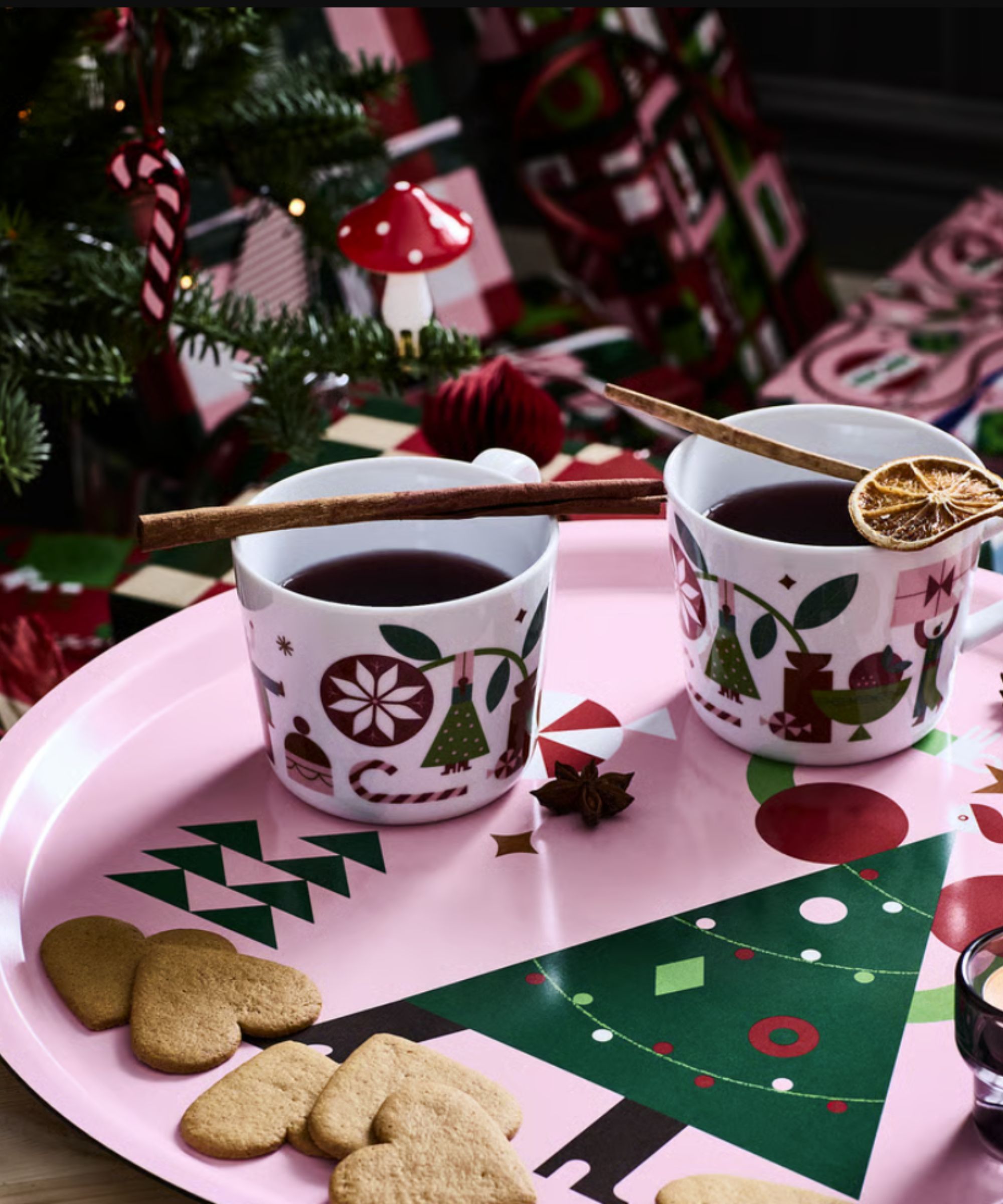 Pink decorative tray with mugs of mulled wine and biscuits on with a Christmas tree behind