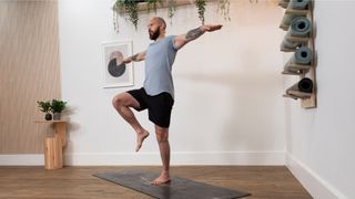 man performing a single leg balance with one knee raised and arms out to the sides