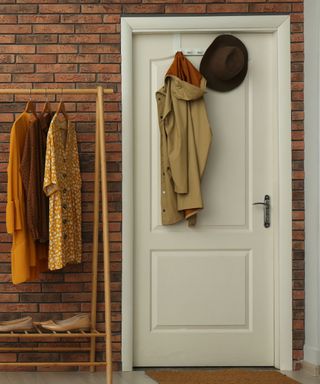 Coats hanging on the back of a white door, an open clothes rack beside it with clothes hanging