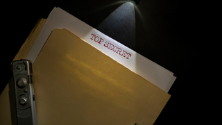 A retro file stamped Top Secret with a camera on top under a spotlight