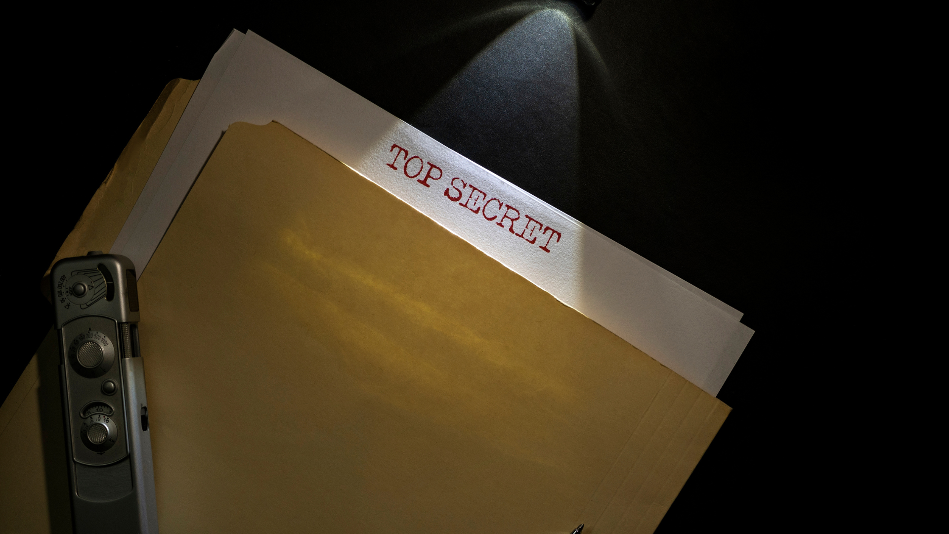 A retro file stamped Top Secret with a camera on top under a spotlight